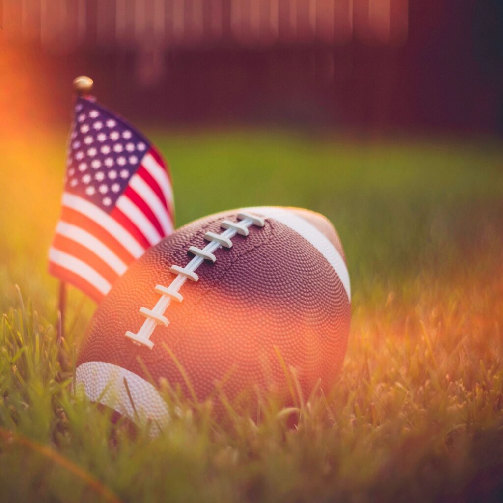 American Football in grass with sun flare and American flag
